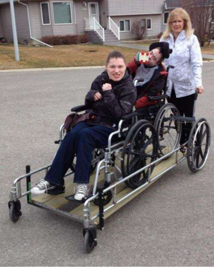 Two people in separate wheelchairs being pushed together on a wheeled platform