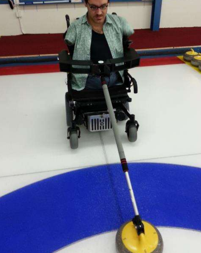 Man in a wheelchair using a pole extension to play curling on ice
