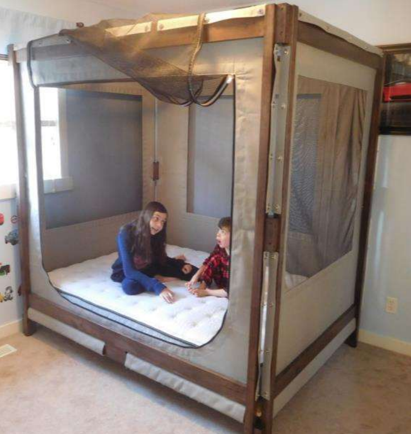 Boy and a girl sitting in a bed that has a surrounding zip up mesh