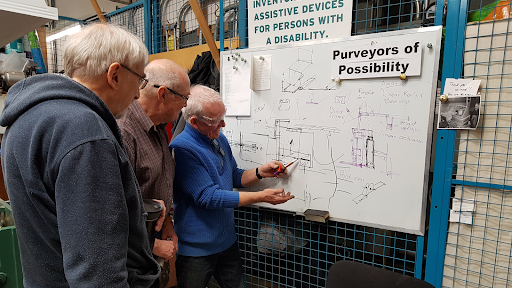 Three men in a workshop looking at schematics on a whiteboard