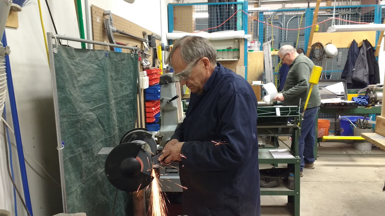 Man in a workshop using a grinding wheel on a piece of metal causing sparks